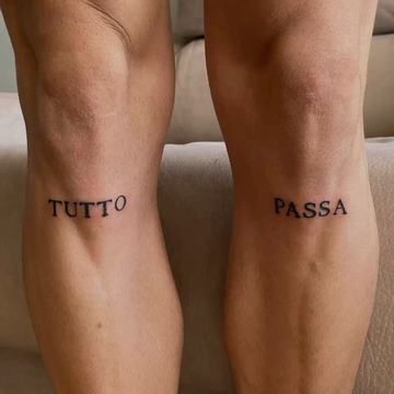 Tatuaje “TUTTO PASSA” en mayúsculas negras, dividido entre ambas pantorrillas; diseño minimalista y legible que simboliza que todo pasa y la superación de etapas.