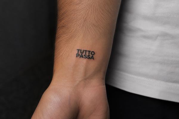 Interior de la muñeca con un tatuaje pequeño en negro que dice “TUTTO PASSA” en mayúsculas, tipografía limpia y minimalista que recuerda que todo pasa.