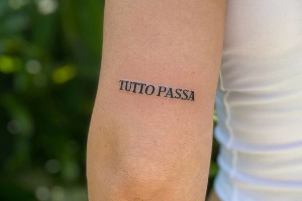 Tatuaje “TUTTO PASSA” en mayúsculas negras
